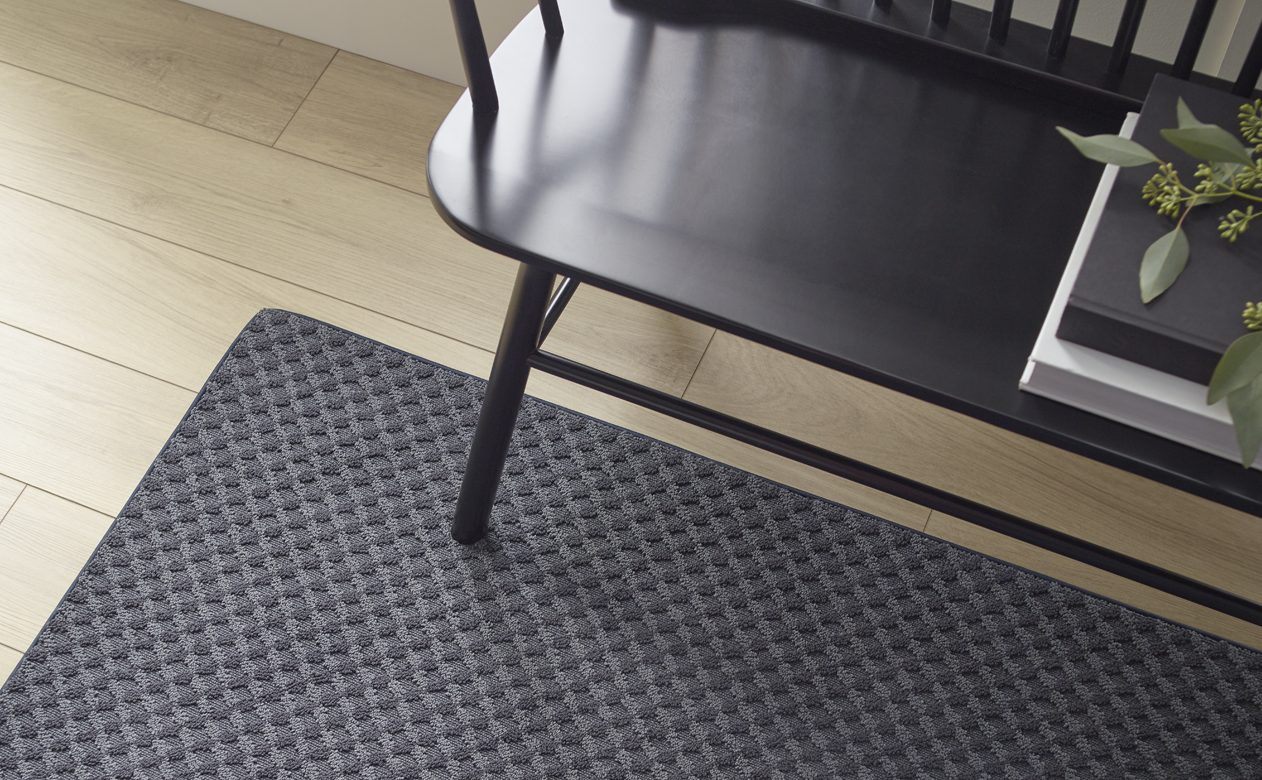 textured dark area rug on light wood floors with black bench